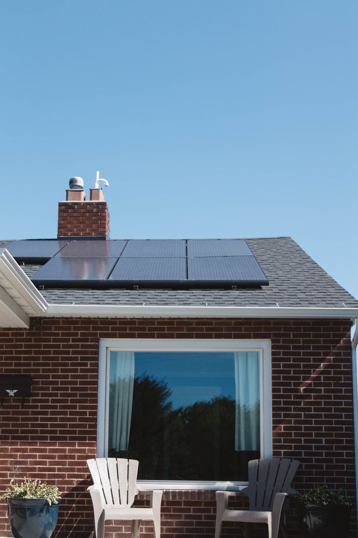 Ziegelhaus mit Solarmodulen auf dem Dach, einem Fenster und zwei Stühlen darunter.
